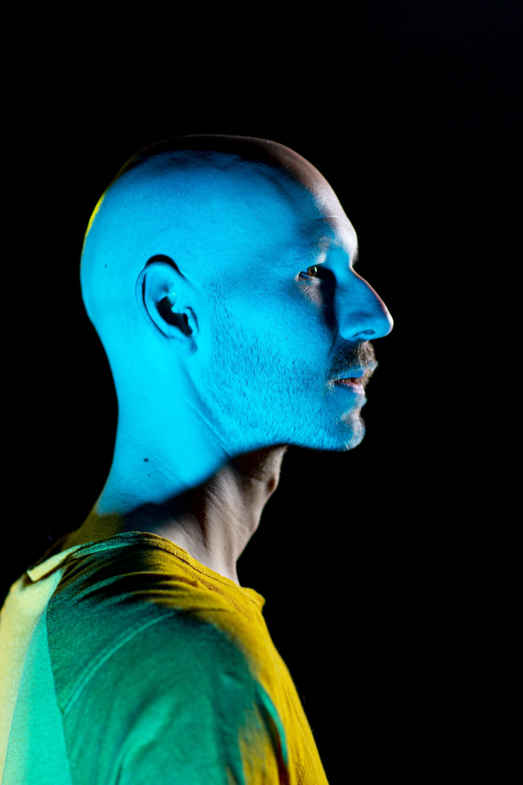 Close Studio Portrait of Timm Roller, wearing a yellow shirt in blue light.